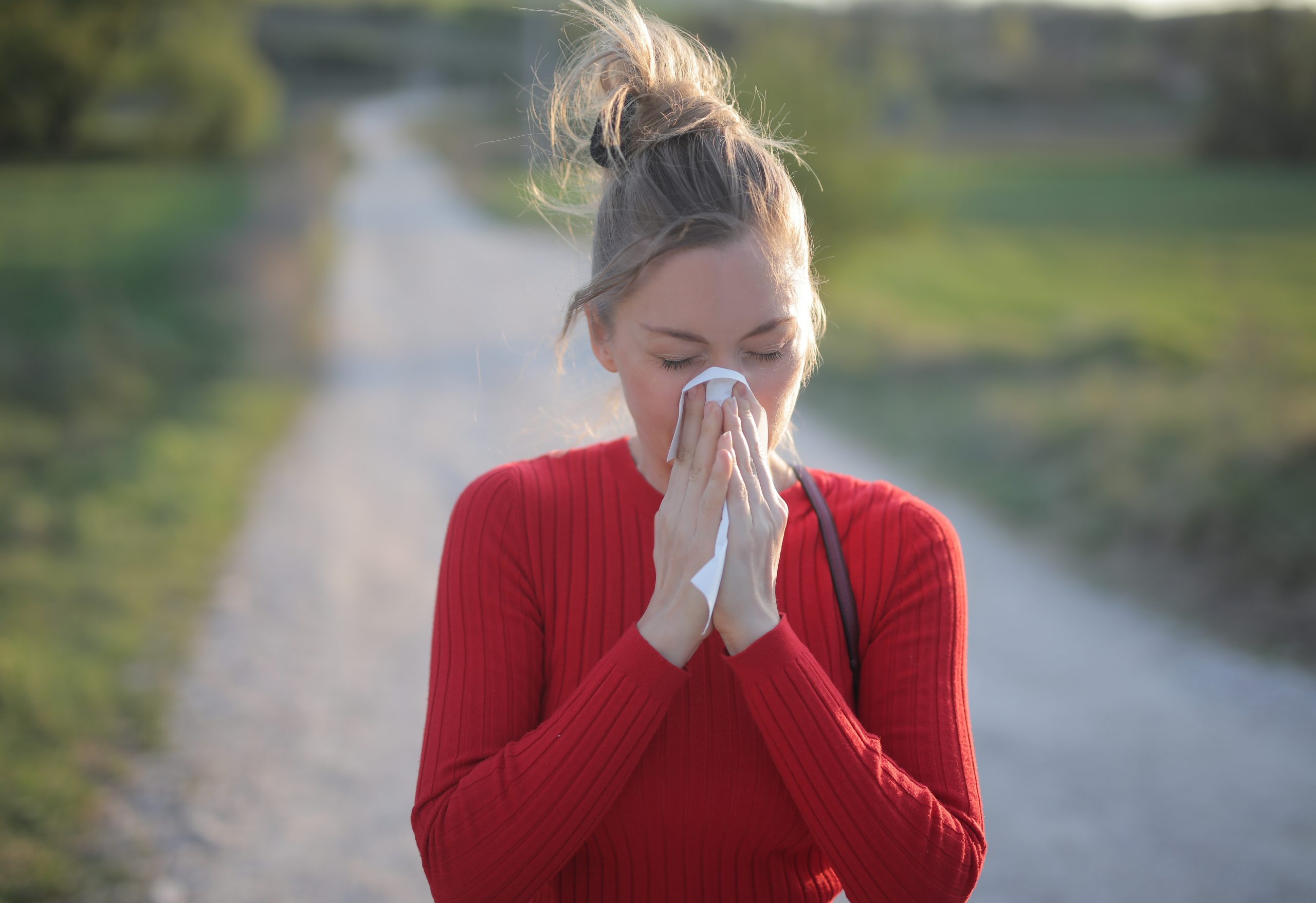 A shallow focus shot of a female wearing red blouse who is having seasonal allergic reactions