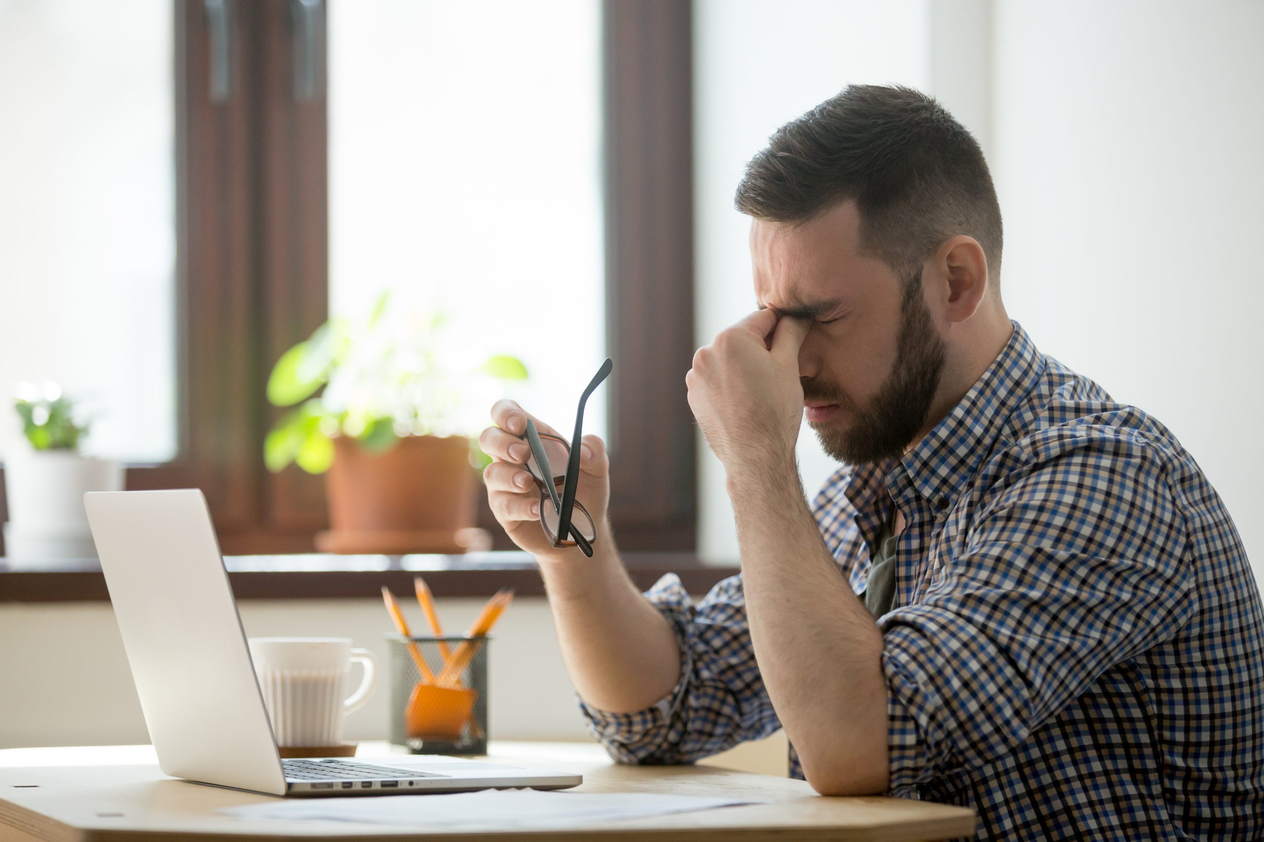 Tired stressed male worker taking off glasses, person massaging nose bridge suffering from headache and trying to relieve pain. Despaired man frustrated after reading company collapse or failure news